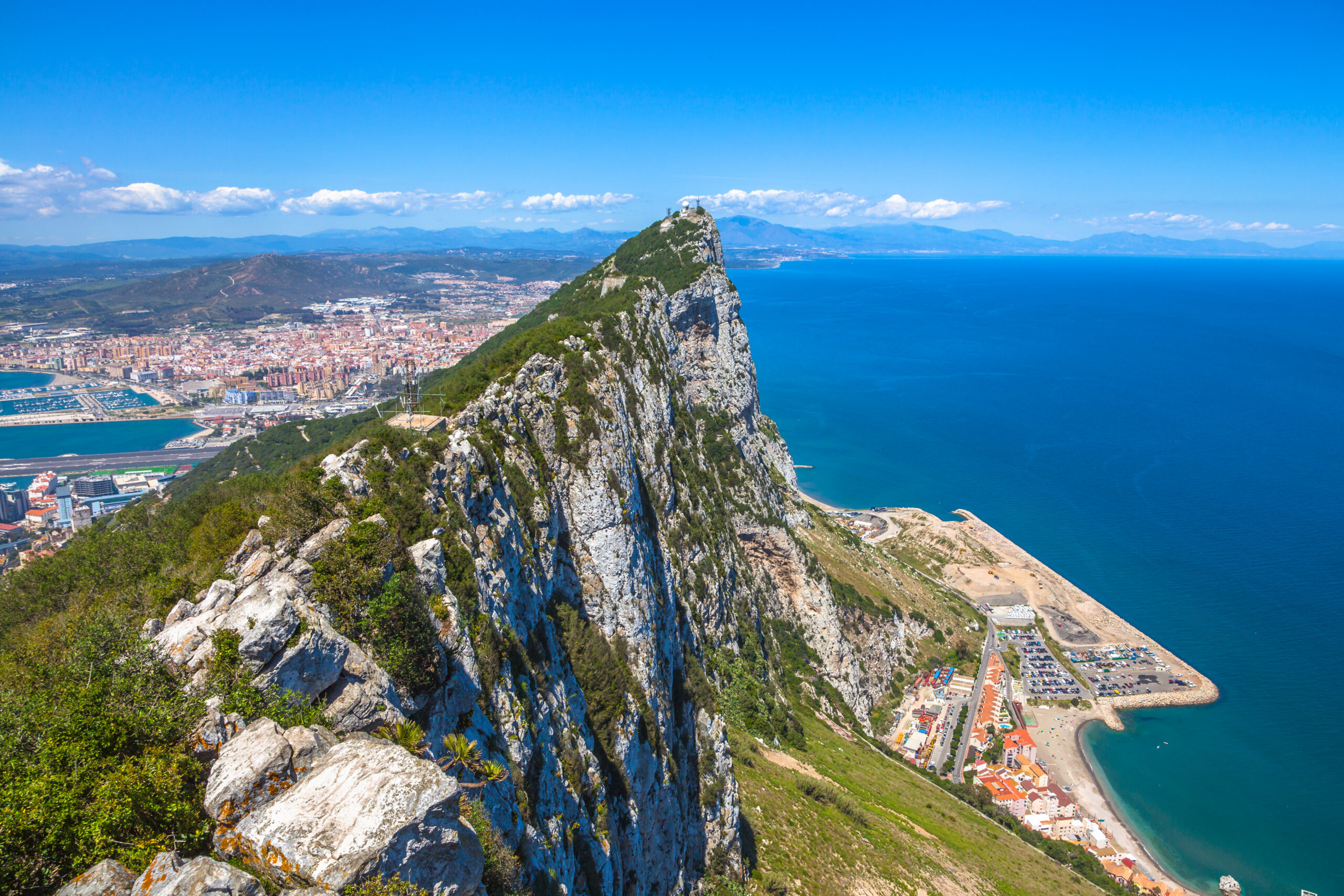 Aerial view of top of Gibraltar Rock, in Upper Rock Natural Reserve: on the left Gibraltar town and bay, La Linea town in Spain at the far end, Mediterranean Sea on the right. United Kingdom, Europe.